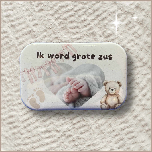 Rechthoekige gepersonaliseerde foto button met de tekst 'Ik word grote zus', babyvoetjes en een knuffelbeer.