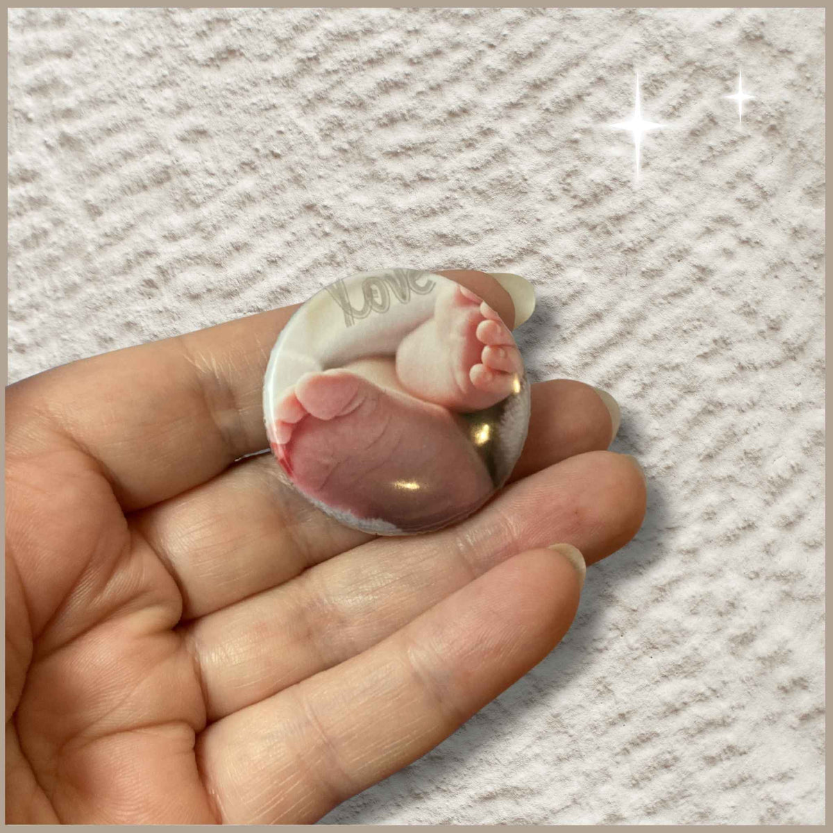 Ronde gepersonaliseerde foto button van 38 mm in een hand met een ontwerp van babyvoetjes en de tekst 'Love'.