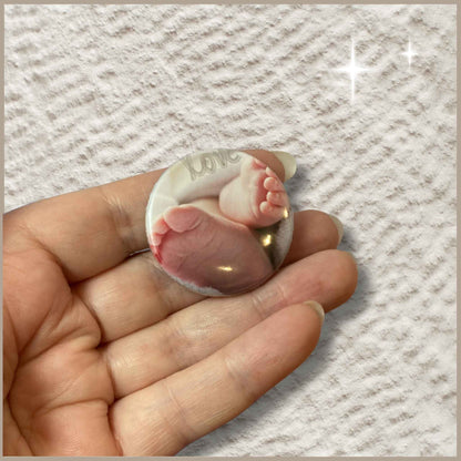 Ronde gepersonaliseerde foto button van 38 mm in een hand met een ontwerp van babyvoetjes en de tekst 'Love'.