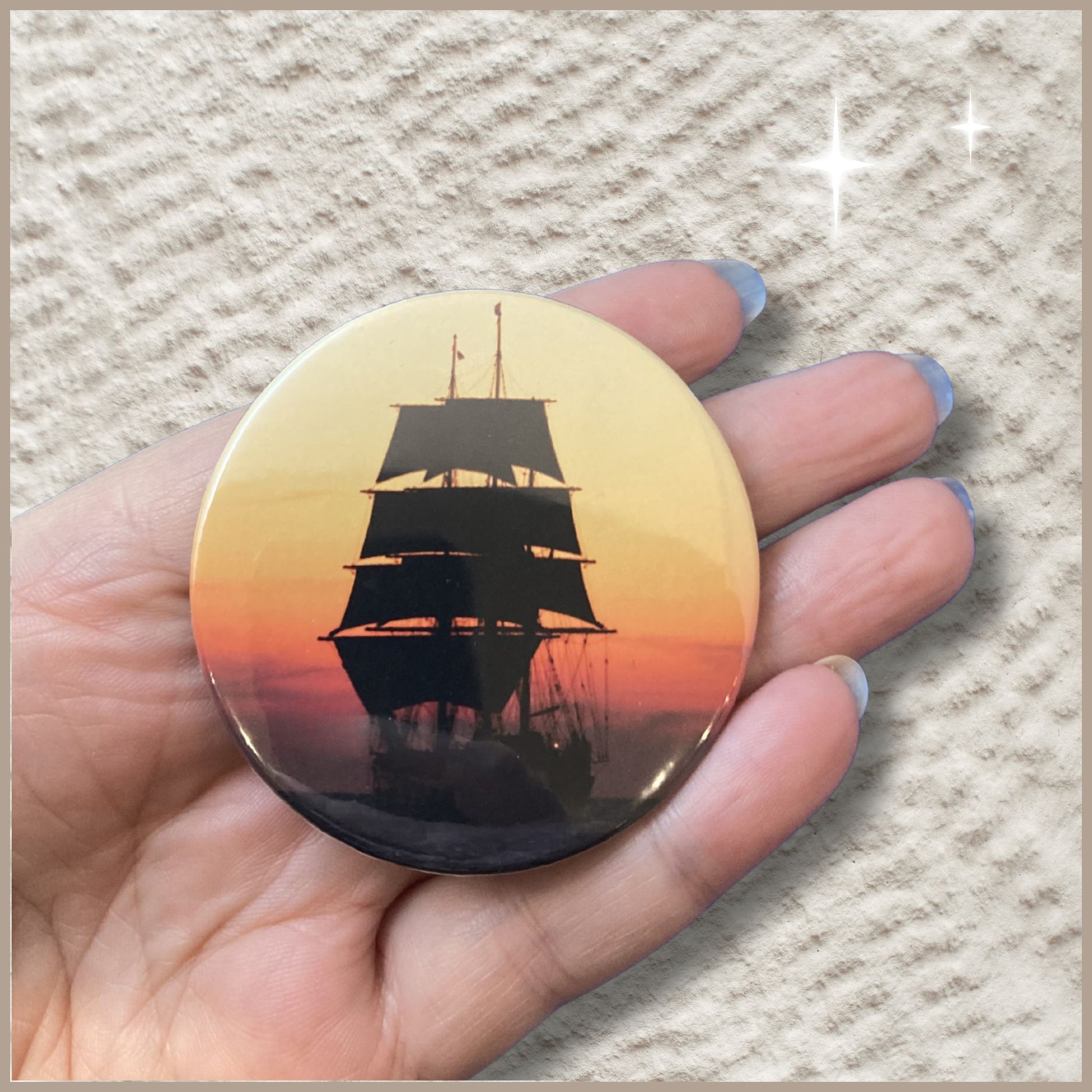 Duidelijke schaalfoto van een ronde gepersonaliseerde fotomagneet van 59 mm met het silhouet van een zeilboot tegen een avondlucht vastgehouden in een hand om het ware formaat te tonen.