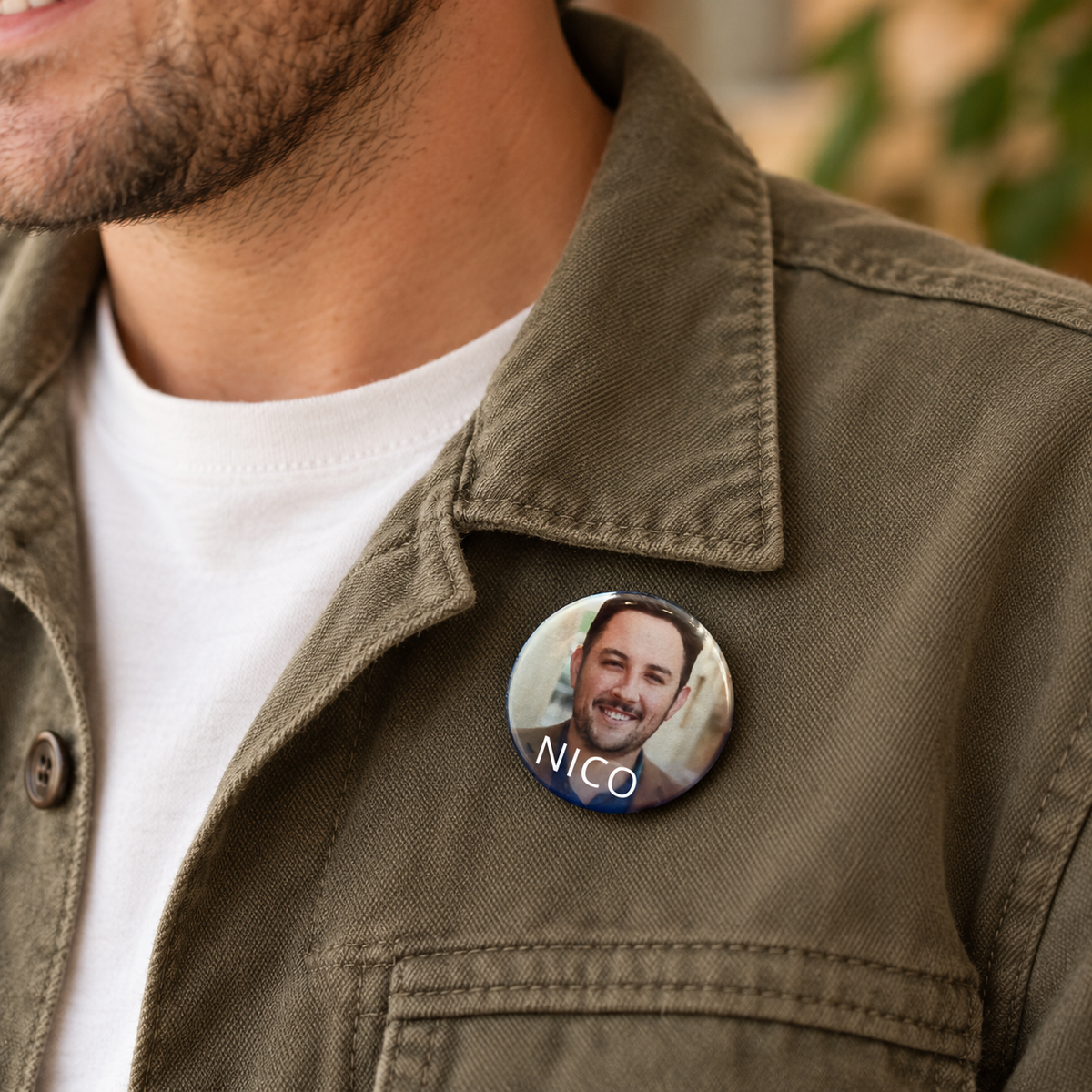Sfeerbeeld van een kleine ronde naambutton van 38 mm met een foto en de naam "Nico", opgespeld op een groen jasje.