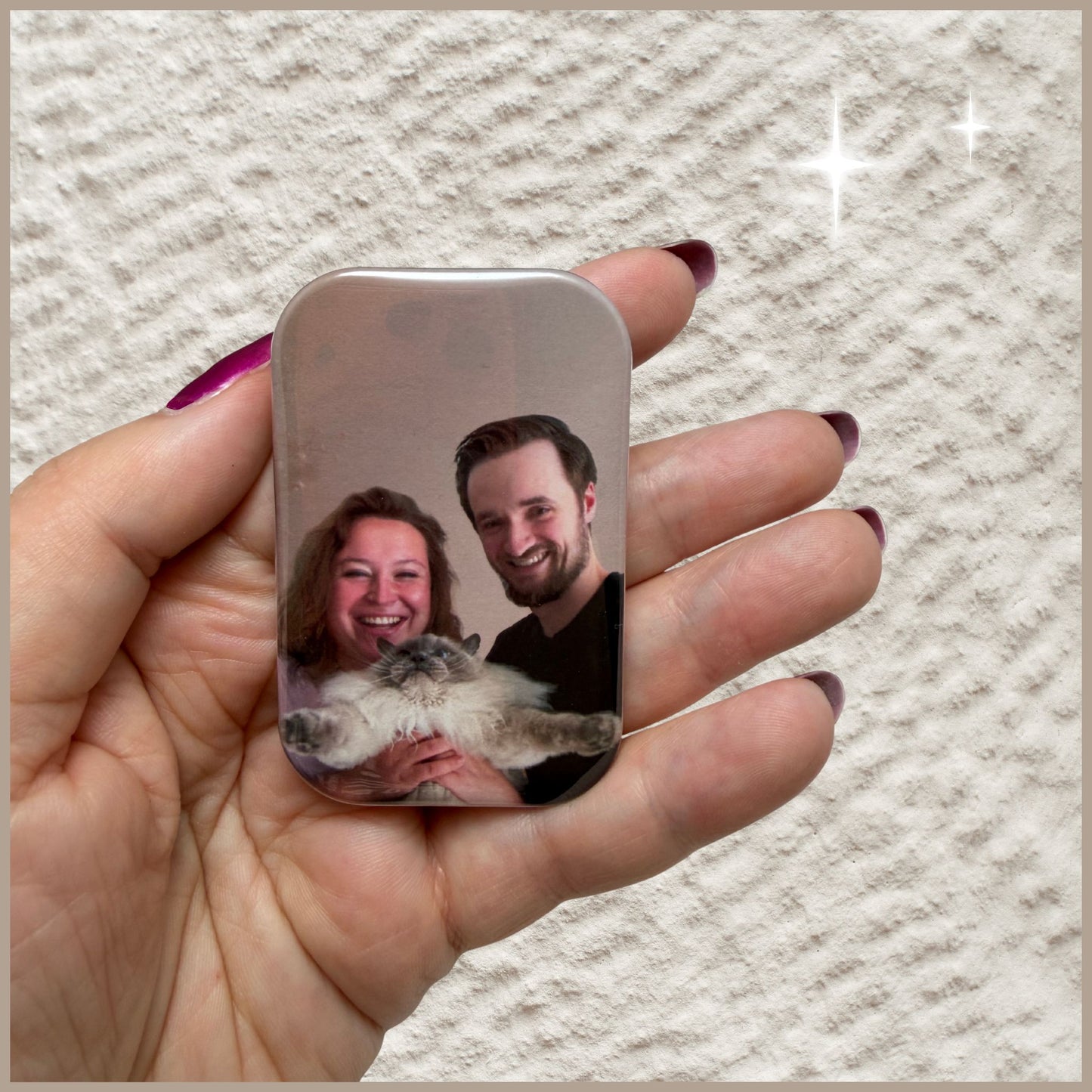 Hand houdt een rechthoekige fotomagneet vast ter indicatie van het formaat, bedrukt met een foto van een lachend koppel en hun kat.