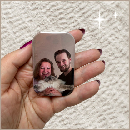 Hand houdt een rechthoekige fotomagneet vast ter indicatie van het formaat, bedrukt met een foto van een lachend koppel en hun kat.