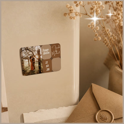 Sfeerfoto van een rechthoekige save-the-date fotomagneet op een koelkast, bedrukt met een foto van een bruidspaar, hun namen en de trouwdatum.